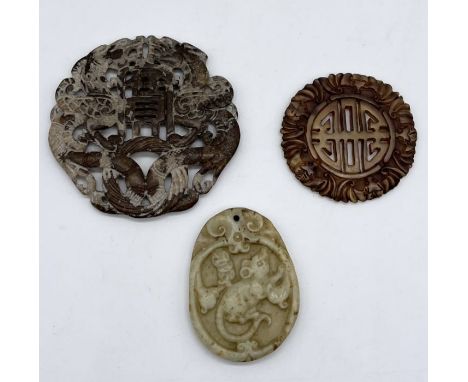 Three carved Chinese pendants/tokens, one larger hardstone example with dragon relief (6.5cm), a smaller jade piece (4.5cm), 