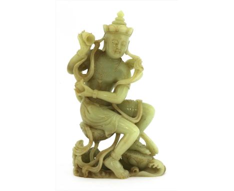 A Chinese jade bodhisattva, wearing beaded jewellery with a cup in both hands, standing on spuming waves with his left foot r