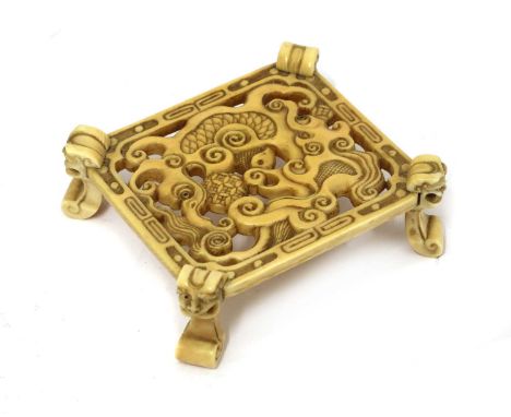 A Chinese ivory stand, early 20th century, of rectangular form on four mask and scroll feet, pierced and carved with two myth