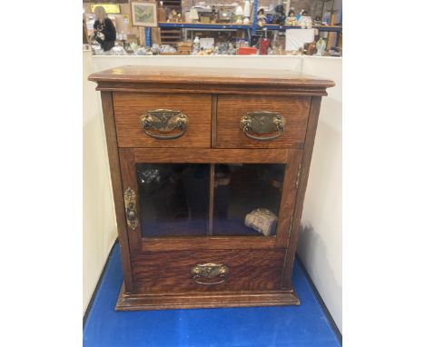 A VINTAGE OAK SMOKERS CABINET WITH TWO SHORT UPPER DRAWERS, A GLAZED DOOR AND A LONG LOWER DRAWER AND TWO VINTAGE PIPES 