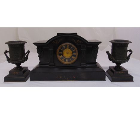 A black slate mantle clock of architectural form flanked by a pair of vase form garnitures