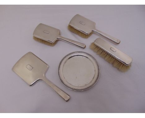 A four piece silver dressing table set to include two hair brushes and a clothes brush a hand mirror and a white metal circul