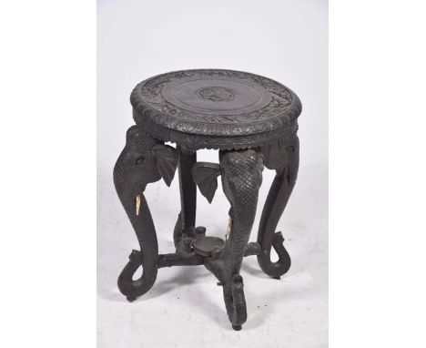 A carved hard wood 'elephant' occasional table The circular top raised on four elephant trunk scroll supports, united by an '