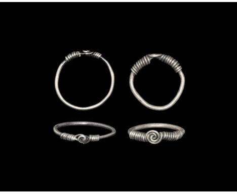 9th-11th century AD. A pair of silver finger rings, each a round-section wire hoop with the ends forming a spiral plaque and 