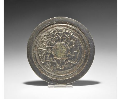 3rd-7th century AD. A flat-section discoid mirror with one polished face, the reverse with concentric raised bands and panel 