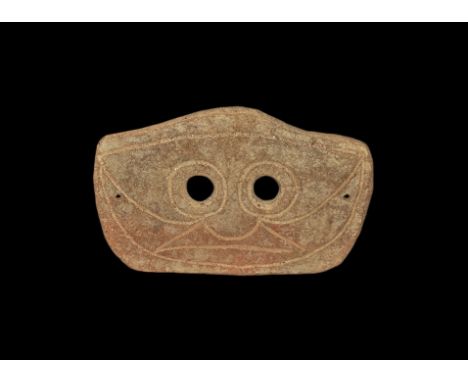 4th-3rd century BC. A rectangular slightly curved ceramic mask with two eye-holes and incised stylised facial details; pierce