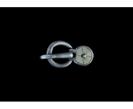 6th century AD. A round-section silver loop and tapering tongue curved over the hoop, discoid silver-gilt plaque with central