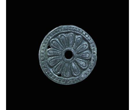 14th-15th century AD. A flat-section silvered bronze disc with central void, twelve radiating petals within a pelletted borde