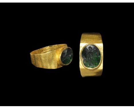 1st-3rd century AD. A gold ring with wide shank and raised bezel holding a green glass intaglio engraved with the image of At