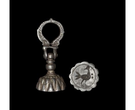 3rd-7th century AD. A silver bell-shaped seal matrix with hinged loop formed as two dolphins; the matrix formed as a chrysant