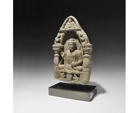 1st-4th century AD. A carved schist panel depicting Buddha seated in a loose robe within an arch, right hand raised in the ge