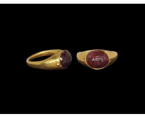 1st-2nd century AD. A D-section gold hoop with expanding shoulders and elliptical plaque, inset garnet cabochon with intaglio