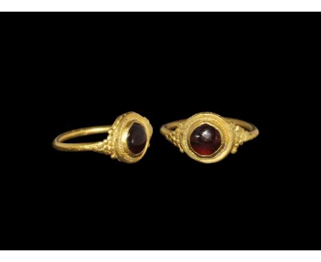 1st-2nd century AD. A round-section hoop supporting a discoid plaque, granulation to the shoulders, wire fillet surrounding t