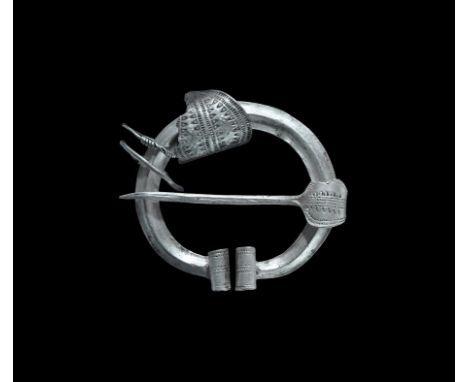 9th-11th century AD. A silver penannular brooch with keeled band and scrolled ends with punched-point detailing, round-sectio