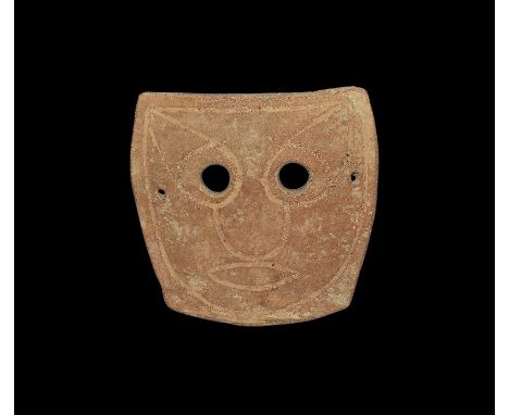 4th-3rd century BC. A heater-shaped slightly domed ceramic mask with two eye-holes and incised stylised facial details; pierc