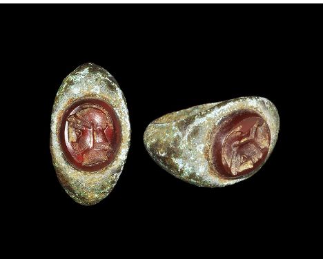 1st-2nd century AD. A D-section hoop and expanding shoulders, flat plaque with inset red glass cloison, intaglio profile bust