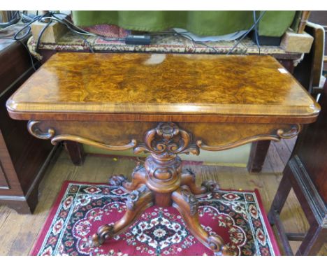 A mid Victorian burr walnut foldover card table, the circular baize interior over a floral carved baluster stem and four flor