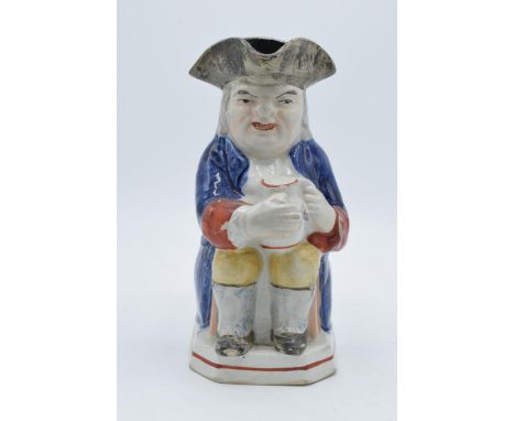 An early 19th century Staffordshire Toby jug of a man in a tricorn hat holding a jug with floral sprays, feet protrude over b