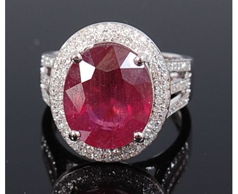 A contemporary 14ct white gold, ruby and diamond set dress ring, arranged as a centre four claw set oval cut ruby weighing ap