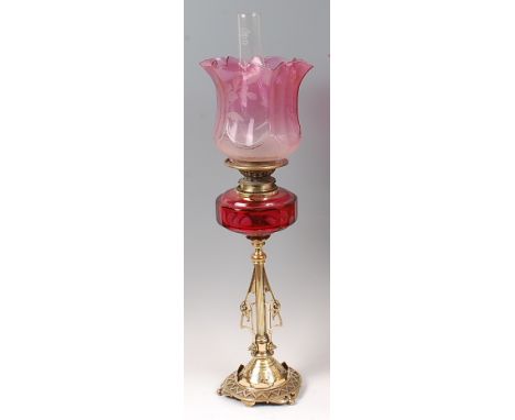 A Victorian brass pedestal oil lamp, having a cranberry tinted and acid etched shade above slab-cut cranberry glass reservoir