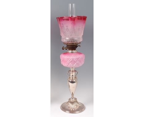 A silver plated pedestal oil lamp, having cranberry tinted acid etched shade and moulded pink glass reservoir to a slender ba