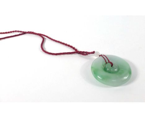 A circular pale green jade pendant of two sections on a cord necklace, d. 5.2 cm