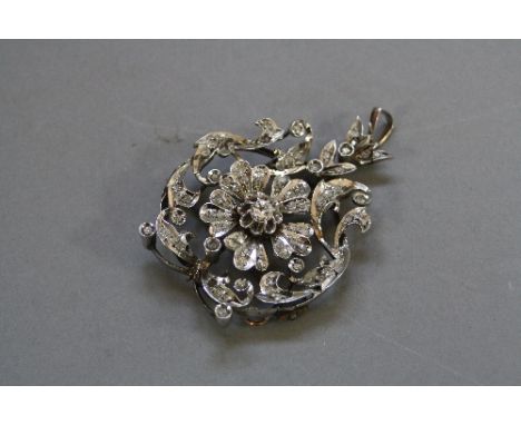 AN EARLY 20TH CENTURY DIAMOND BROOCH PENDANT, a fancy floral and scroll open work design, centring on a transitional brillian