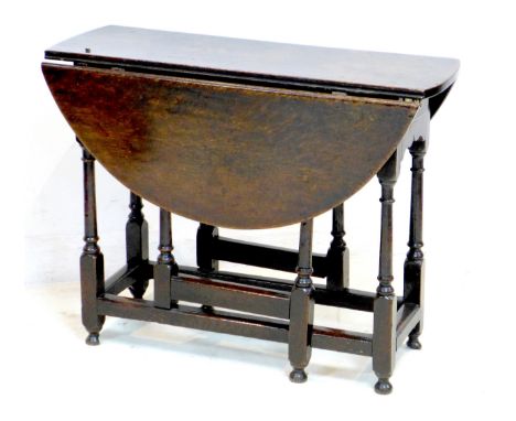 An 18th century oak drop leaf table, with oval surface, twin gate leg action, raised on turned supports joined by stretchers,