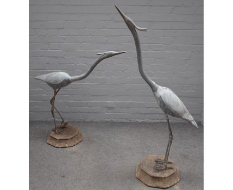 Two architectural lead garden figures of herons, on octagonal reconstituted stone bases, 139cm high and 104cm high, (2).
