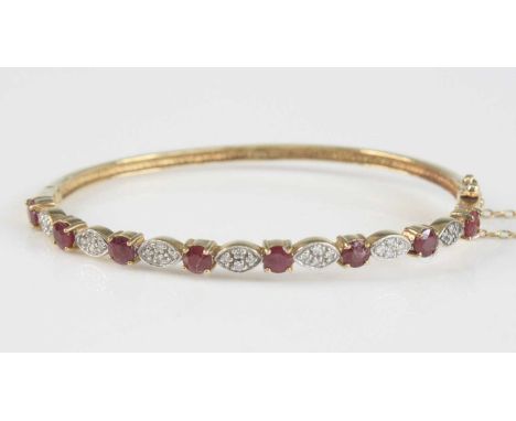A 9ct yellow gold, ruby and diamond hinged oval hollow bangle, featuring eight round faceted rubies alternating with seven le