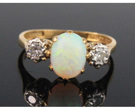 A yellow and white metal, opal and diamond three stone ring, featuring a centre oval opal cabochon with a round brilliant cut