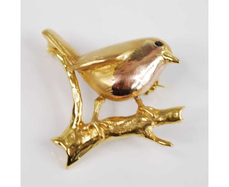 A 9ct yellow gold brooch depicting a robin on a branch with rose gold detail for the breast and a 1.8mm blue stone for the ey