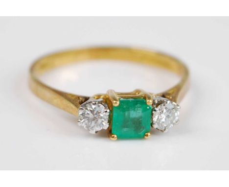 An 18ct yellow and white gold emerald and diamond three stone ring featuring a centre octagonal emerald with a round brillian