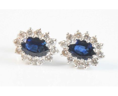 A pair of 18ct white gold, sapphire and diamond oval cluster earrings, each featuring a centre oval sapphire within a border 