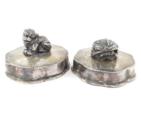 Two Chinese white metal covers, serpentine borders, each with a shishi and dragon ball finial, 9cm diameter
