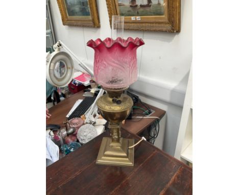 A Victorian brass based oil lamp with floral cranberry shade, converted to electricity, 62cm tall