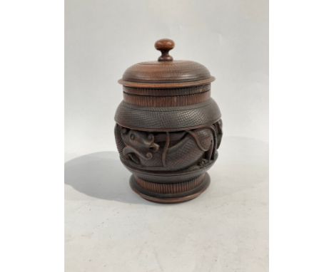 A carved wood Oriental tobacco jar with carved decoration of serpents, lid with finial knop, 18cm high 