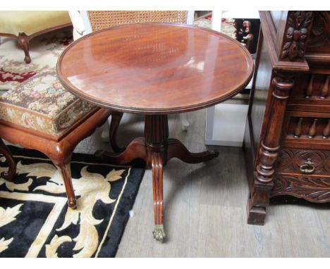 A 19th Century mahogany wine table, the dished top over a fluted column to a tripod base with brass lion paw feet and castors