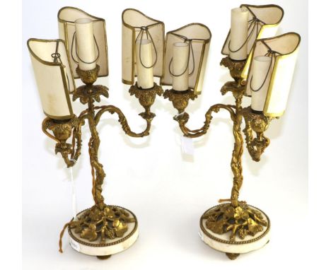 A pair of gilt metal three-light candelabra, late 19th century, cast with fruiting vine on circular white marble bases and pe