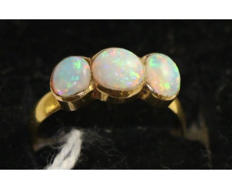 An opal three stone ring, a round cabochon opal between two oval cabochon opals in yellow rubbed over settings, on a plain po