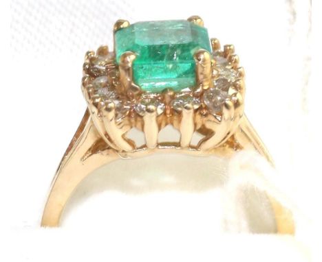 An emerald and diamond cluster ring, an emerald-cut emerald within a border of round brilliant cut diamonds, in yellow claw s