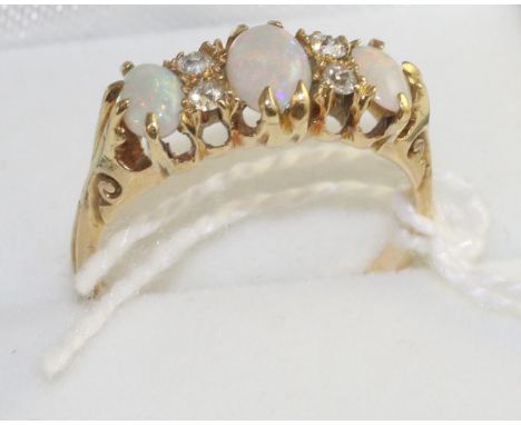 An opal and diamond ring, three graduated oval cut opals spaced by old cut diamonds in a yellow carved setting, to scroll sho