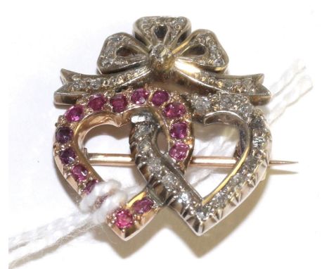 A ruby and diamond twin heart brooch, one heart set with round cut rubies in yellow claw settings, entwinned with a second he