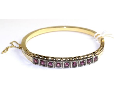 A ruby bangle, nine round cut rubies in white milgrain box settings, above a pierced gallery, to a yellow plain hinged back T