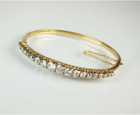 A late 19th century diamond hinged bangle, designed as twenty graduated old cut diamonds claw set in yellow metal, with box c