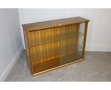 A vintage teak-effect laminate bookcase with sliding glass doors and glass shelving 79cm x 107cm x 29.5cm some minor marks, o