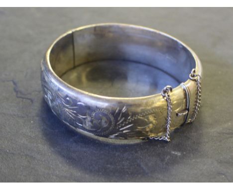 A silver bangle, of hinged circular form with foliate engraving, 7cm, 29grams, tarnishing, generally good.