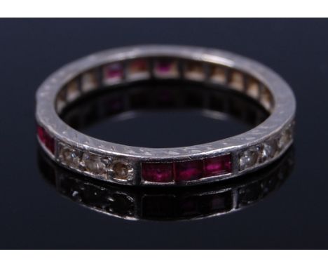 An 18ct white gold, ruby and diamond set eternity ring, the band set with alternating groups of three square cut rubies and t