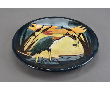 A Moorcroft Pottery ceramic charger, in the Heron pattern depicting a colourful bird with an evening catch of eel, impressed 