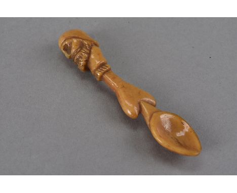 An amber colour carved bone spoon, the heart shaped shaft surmounted by a carved head terminal with eye patch, possibly 18th 